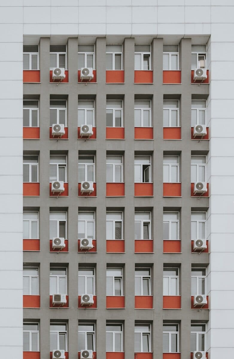 Grey building facade with red window accents and air conditioners